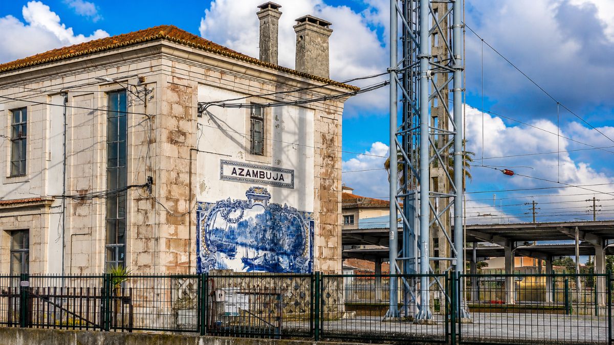 Fachada lateral do edifício da antiga estação de trem de Azambuja em Portugal exibindo um grande painel decorativo de azulejos azuis e brancos com cenas históricas e ribeirinhas abaixo da placa com o nome do município.