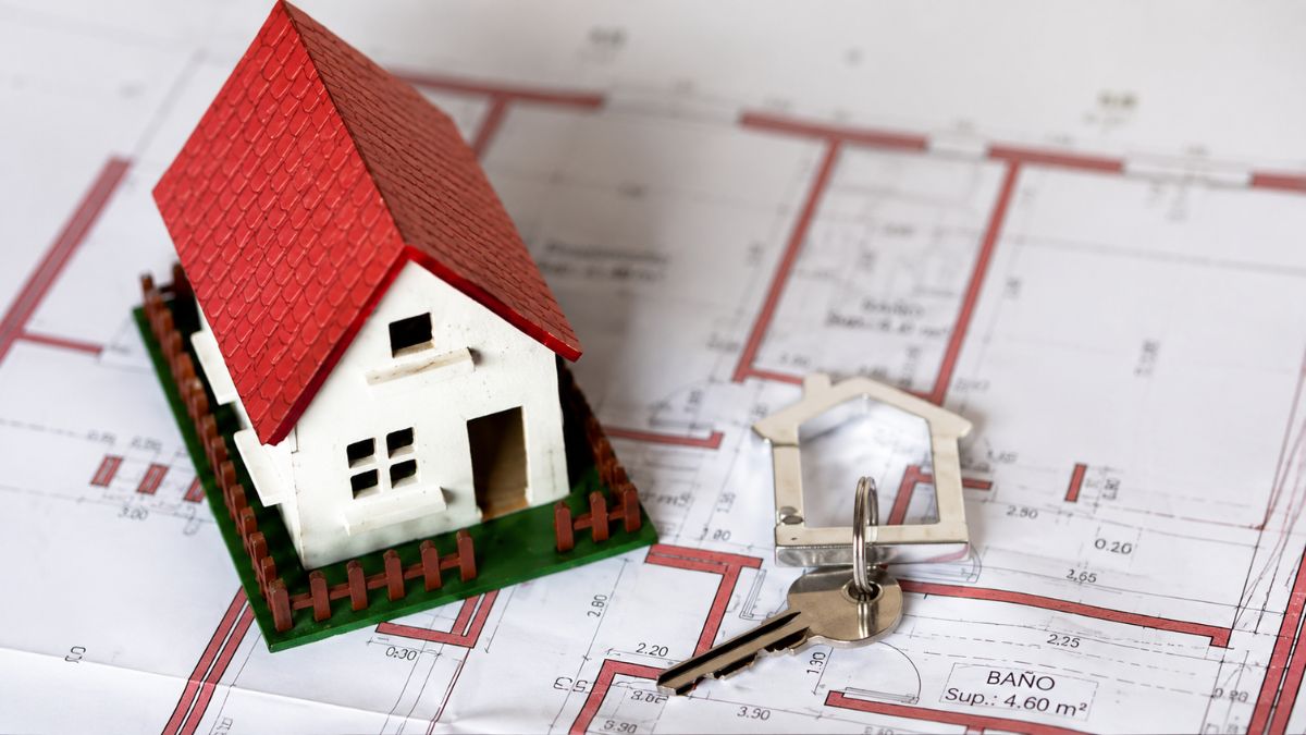Miniatura de casa com telhado vermelho e chave de metal posicionadas sobre a planta baixa de um projeto imobiliário de arrendamento em Arruda dos Vinhos.