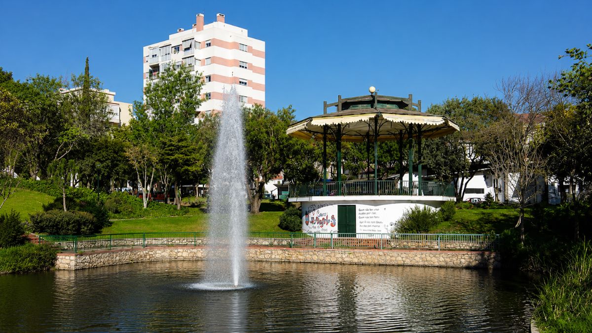 Vista do Parque Delfim Guimarães com o seu lago, chafariz central e o coreto histórico em um dia ensolarado na cidade da Amadora.