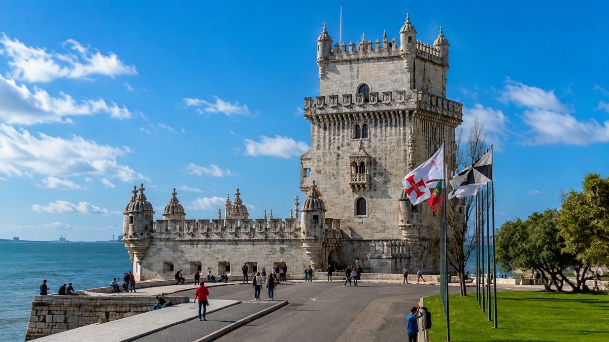Torre de Belém em Lisboa com turistas caminhando na área externa do monumento histórico perto do Rio Tejo sob céu azul com nuvens em Portugal.