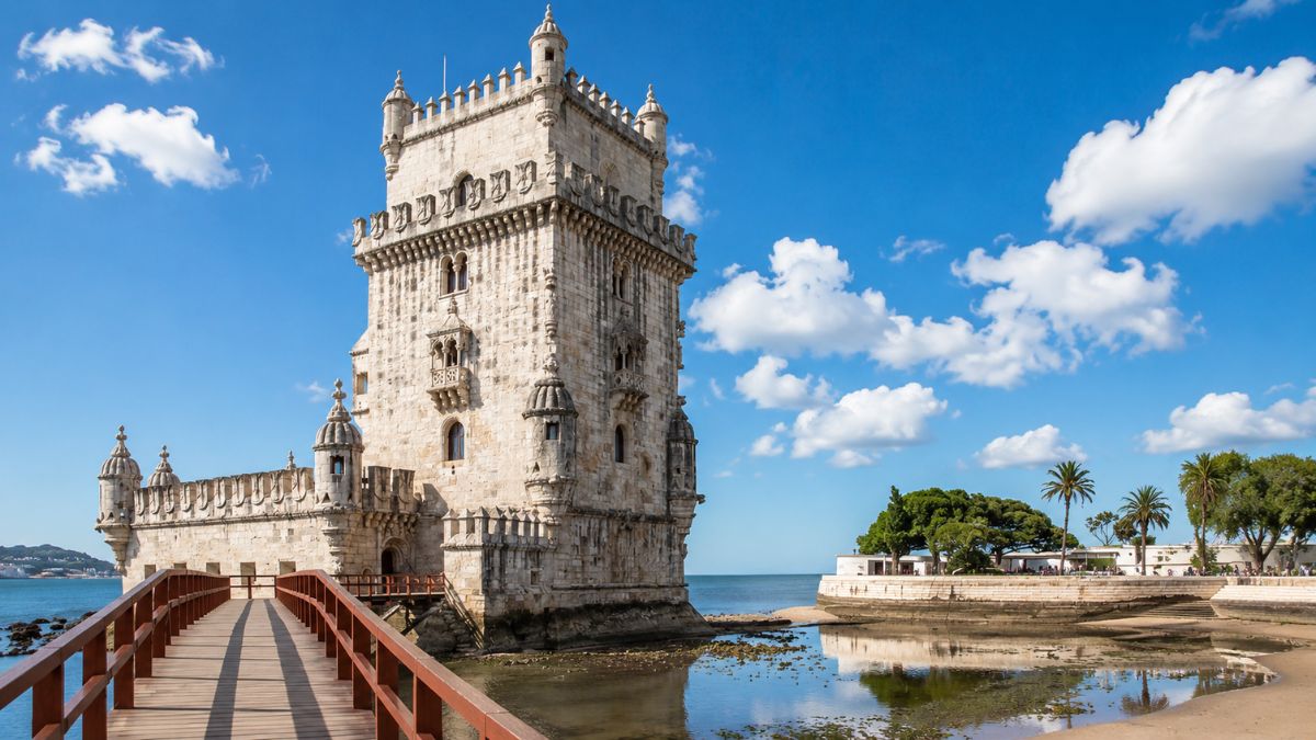 Vista da histórica Torre de Belém em Lisboa com sua ponte de madeira sobre o Rio Tejo em um dia ensolarado.