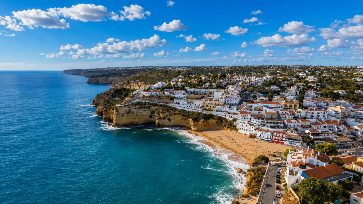 Vista aérea da praia de Carvoeiro no Algarve em Portugal mostrando casas brancas sobre falésias banhadas pelo mar azul.