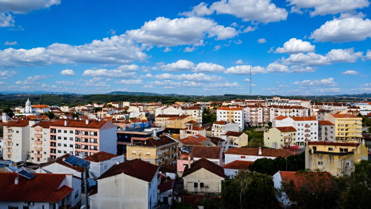 Fotografia colorida com vista aérea de edifícios residenciais com telhados de cerâmica vermelha sob céu azul com nuvens na vila de Cadaval em Portugal.