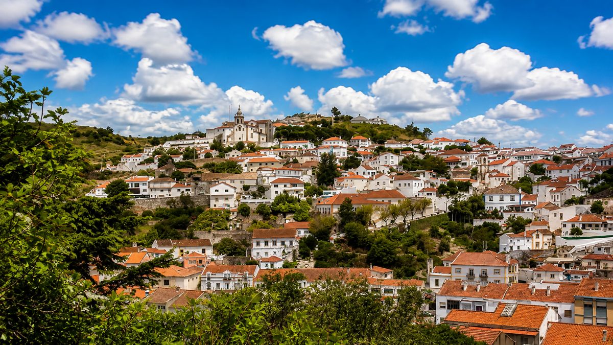 Fotografia panorâmica das casas brancas com telhados vermelhos na encosta histórica da pacata Vila de Alenquer sob céu ensolarado em Portugal.