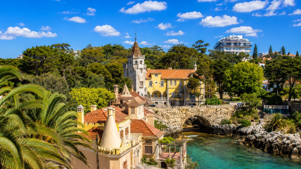 Palácio dos Condes de Castro Guimarães em Cascais com arquitetura medieval e ponte de pedra sobre águas cristalinas do mar.