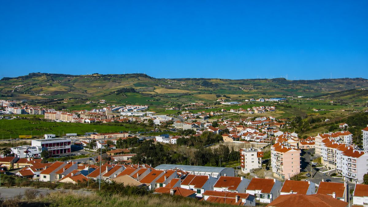 Fotografia aérea colorida mostrando o vale de Arruda dos Vinhos com casas de telhado de azulejo laranja sob um céu azul claro.