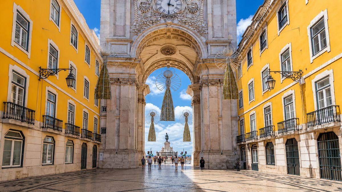 Vista interna através do Arco da Rua Augusta revelando a Praça do Comércio com a estátua de Dom José I ao fundo sob céu azul em Lisboa.
