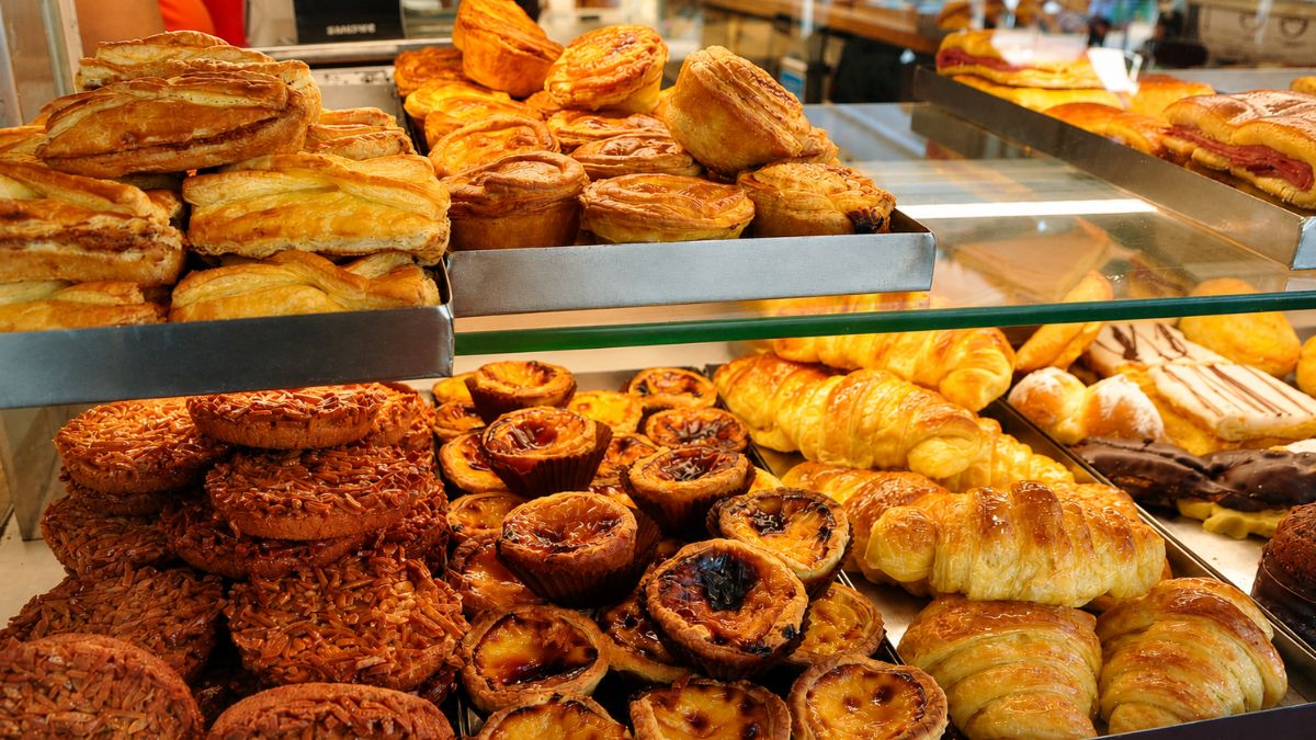 Vitrine de confeitaria tradicional no Porto repleta de doces portugueses com destaque para pastéis de nata caramelizados, croissants dourados e jesuítas folhados.