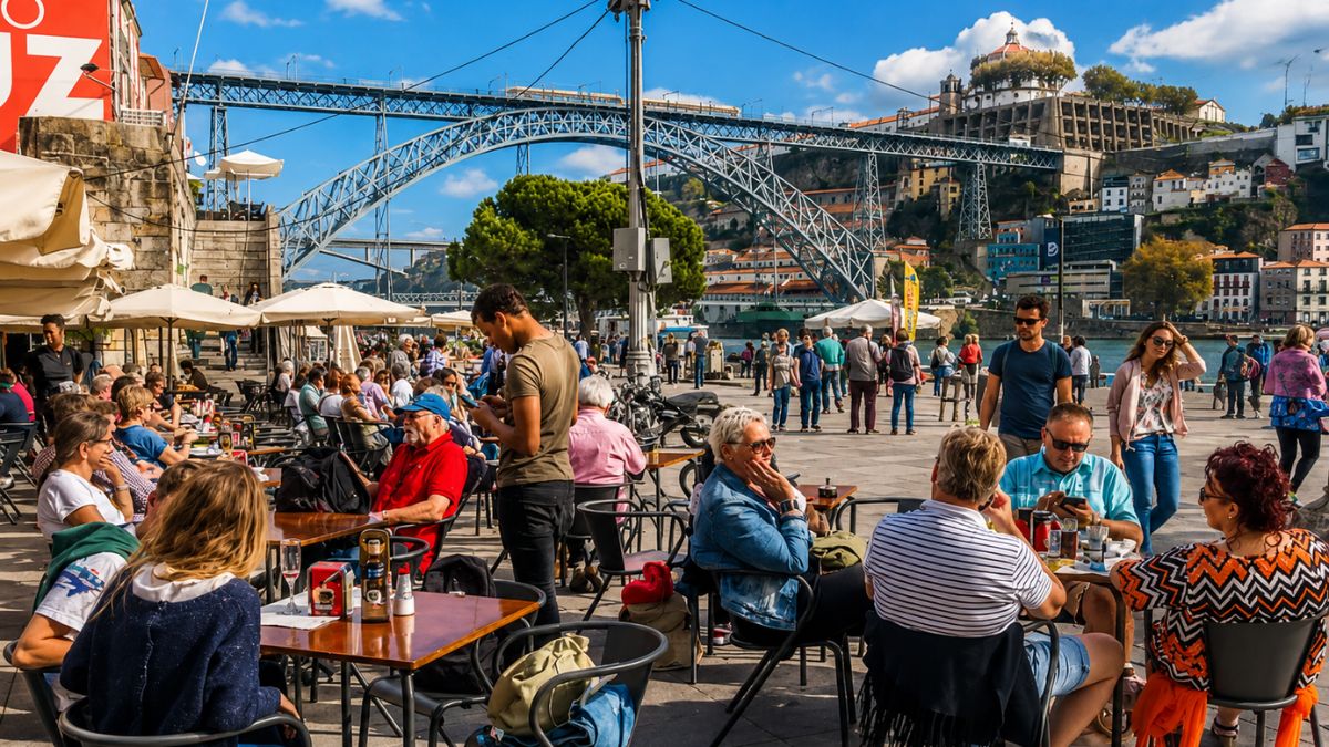 Mesas ao ar livre de restaurantes na Ribeira com clientes sentados e a icônica Ponte Luís I ao fundo.