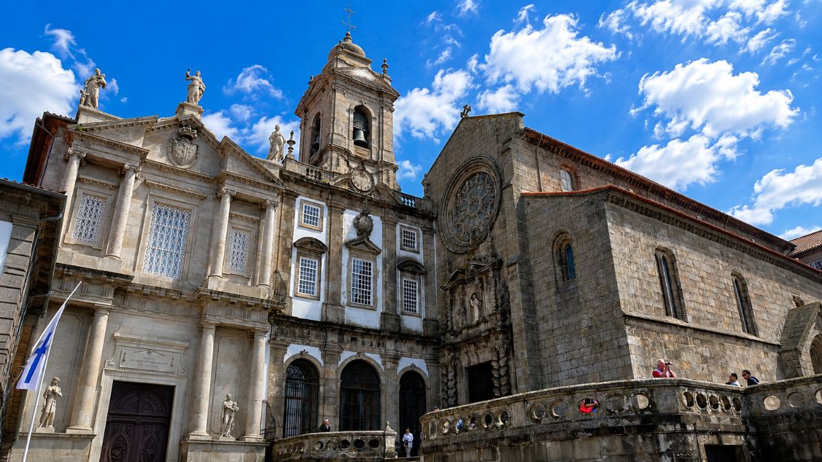 Fachada exterior em estilo gótico e barroco da Igreja de São Francisco exibindo uma grande rosácea de pedra ao lado de uma torre sineira sob céu azul.