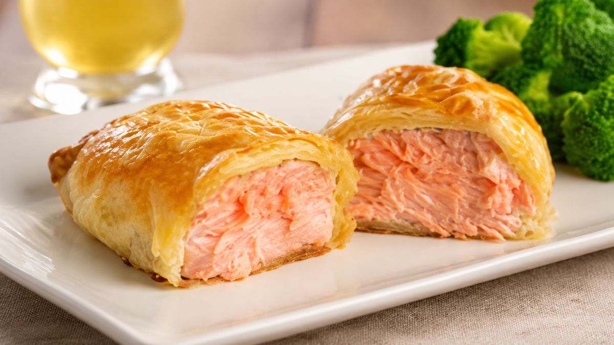 Folhado de salmão assado com massa folhada dourada e crocante, servido em prato branco com brócolis ao fundo.