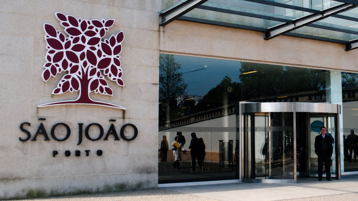 Fachada moderna do Hospital de São João com logotipo na parede de pedra e porta giratória de vidro na cidade do Porto