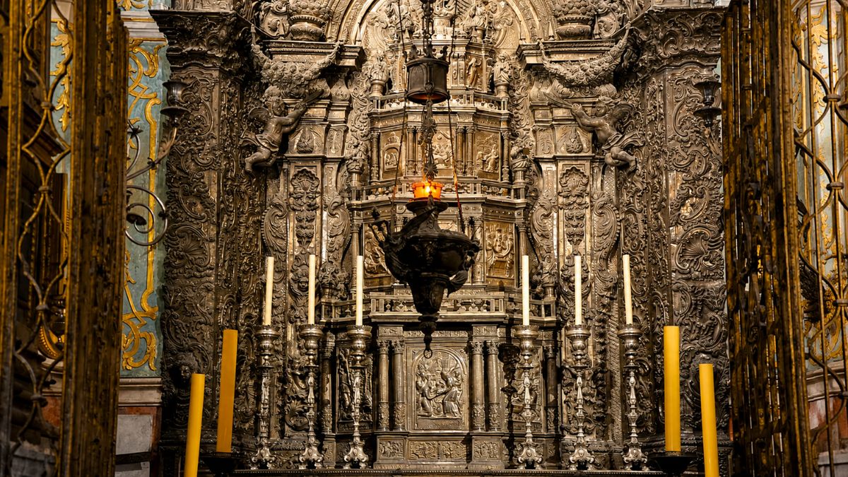 Vista em detalhe do Altar de Prata na Capela do Santíssimo Sacramento da Catedral da Sé do Porto, exibindo o retábulo monumental de prata cinzelada com esculturas de anjos, altos-relevos sacros, grandes velas amarelas e uma lâmpada votiva suspensa em primeiro plano.
