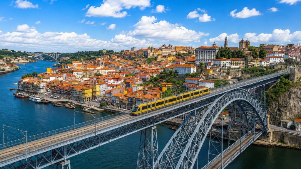Ponte Dom Luís I em Porto com metrô amarelo cruzando o tabuleiro superior sobre o Rio Douro e vista da cidade.