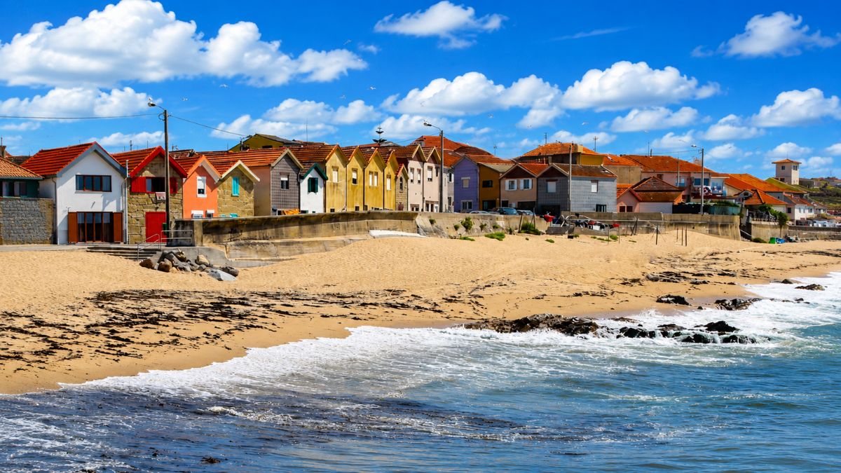 Casas coloridas de pescadores alinhadas na areia da praia de Vila Chã em Vila do Conde sob céu azul.
