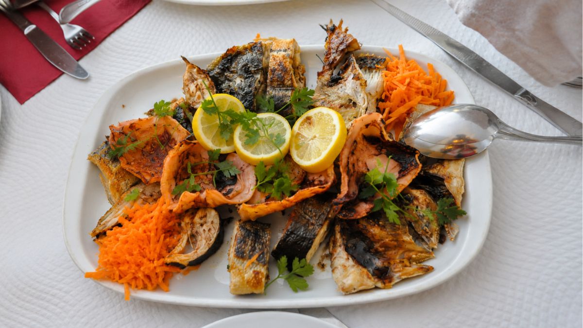 Travessa de bacalhau e peixes grelhados na brasa com rodelas de limão, cenoura ralada e salsa em restaurante de Matosinhos.