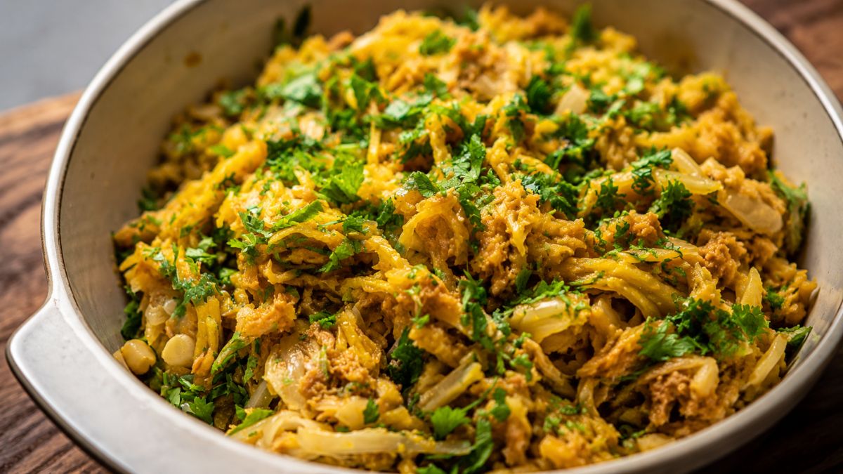 Uma tigela de cerâmica rústica contém Atum à Brás, um prato tradicional português com atum desfiado, batata palha fina, cebola caramelizada e ovos cremosos, tudo finalizado com salsa picada fresca.