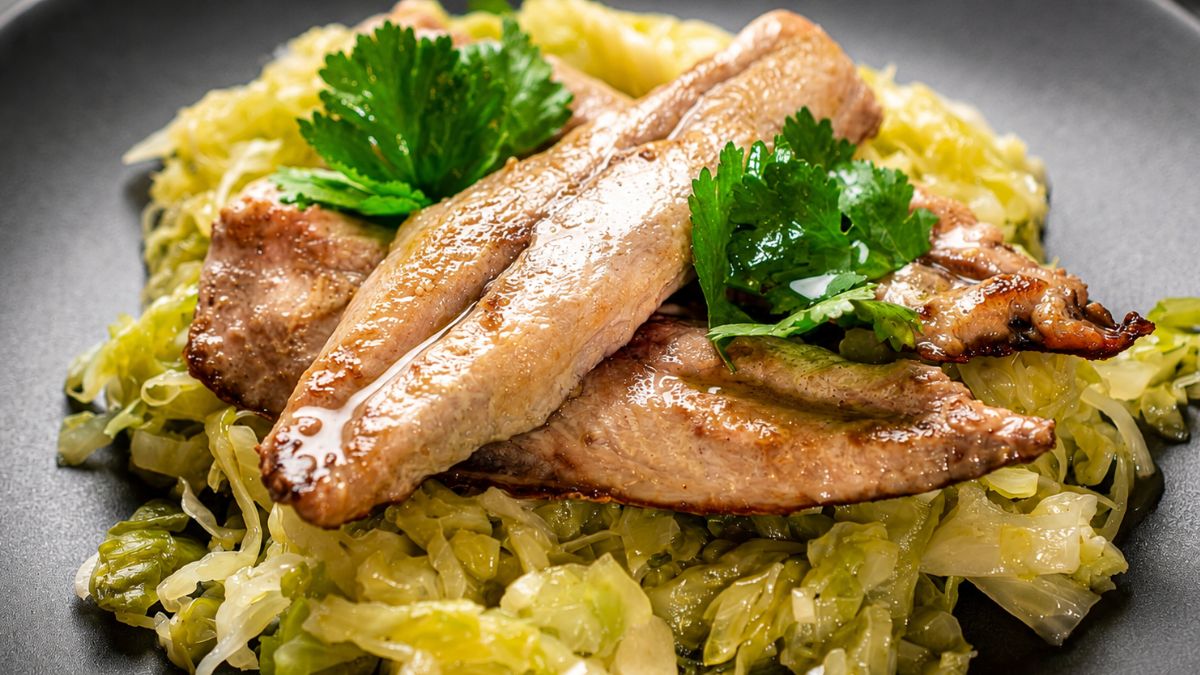 Uma foto close up bem iluminada de filetes de cavala grelhados e suculentos sobre uma cama de couve salteada verde clara e picada, decorada com coentros frescos em um prato preto.