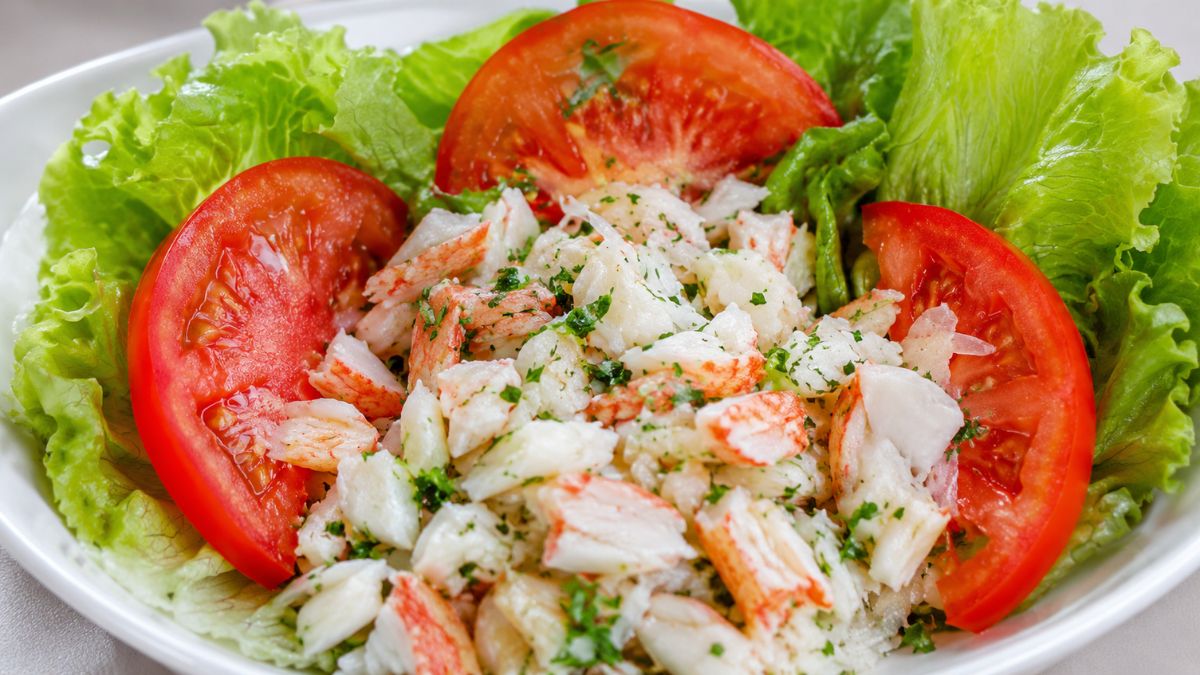 Prato de salada de lagosta com pedaços do marisco temperados com coentro, acompanhados de fatias de tomate e folhas de alface.