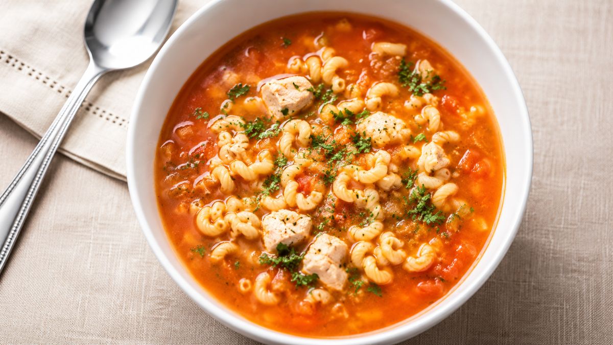 Sopa de peixe cremosa com massa cavatappi, cubos de peixe branco e coentros picados em uma tigela branca sobre toalha de linho, acompanhada por colher.