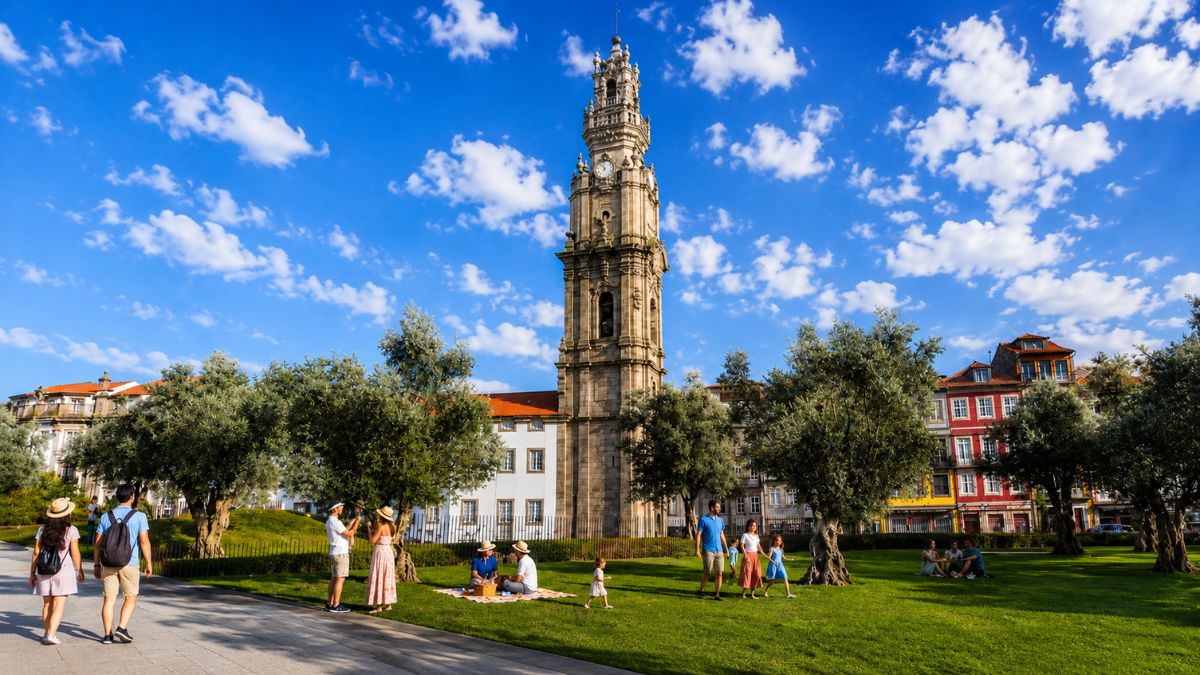 Vista da Torre dos Clérigos no Porto a partir de um gramado verde com árvores e pessoas aproveitando o dia.