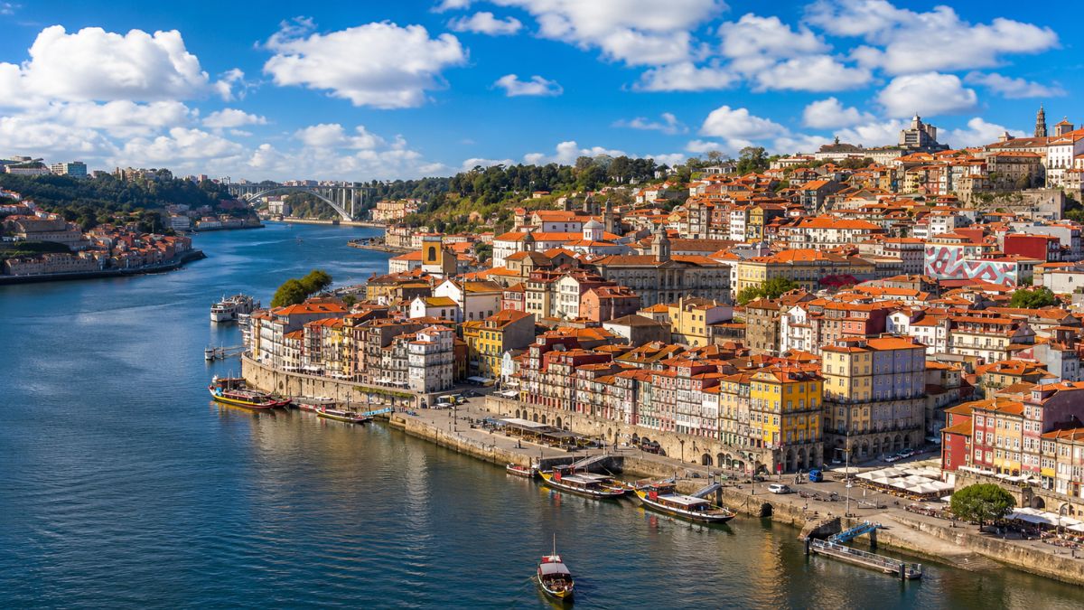 Vista aérea da Ribeira no Porto com casario colorido, barcos rabelos no Rio Douro e Ponte da Arrábida ao fundo.