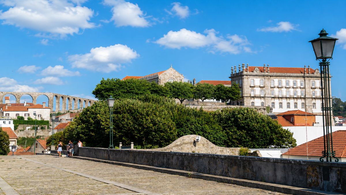 Fotografia urbana de Vila do Conde destacando o histórico Convento de Santa Clara e os arcos de pedra do antigo aqueduto sob céu ensolarado.