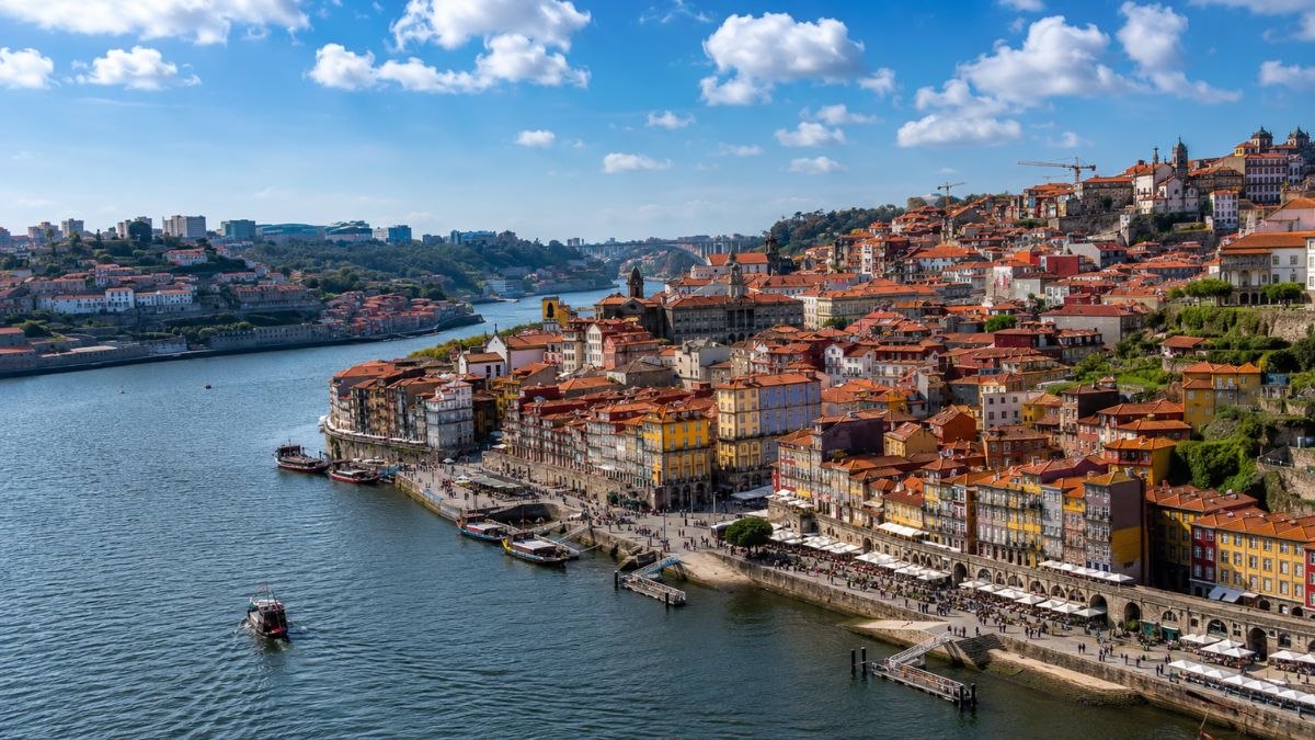 Vista aérea da cidade do Porto mostrando o bairro histórico da Ribeira com casario colorido na margem do Rio Douro no norte de Portugal sob céu azul com nuvens.