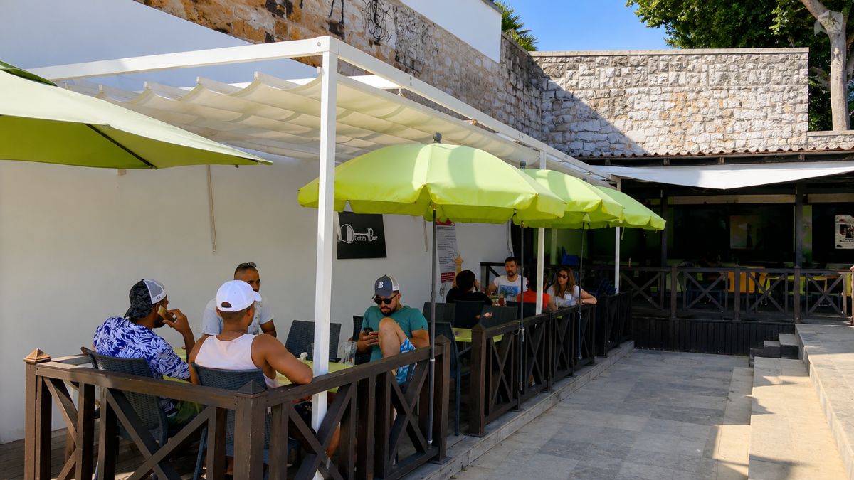 Pessoas acomodadas sob guarda-sóis na esplanada externa do Duche Bar perto da Praia da Duquesa em Cascais.