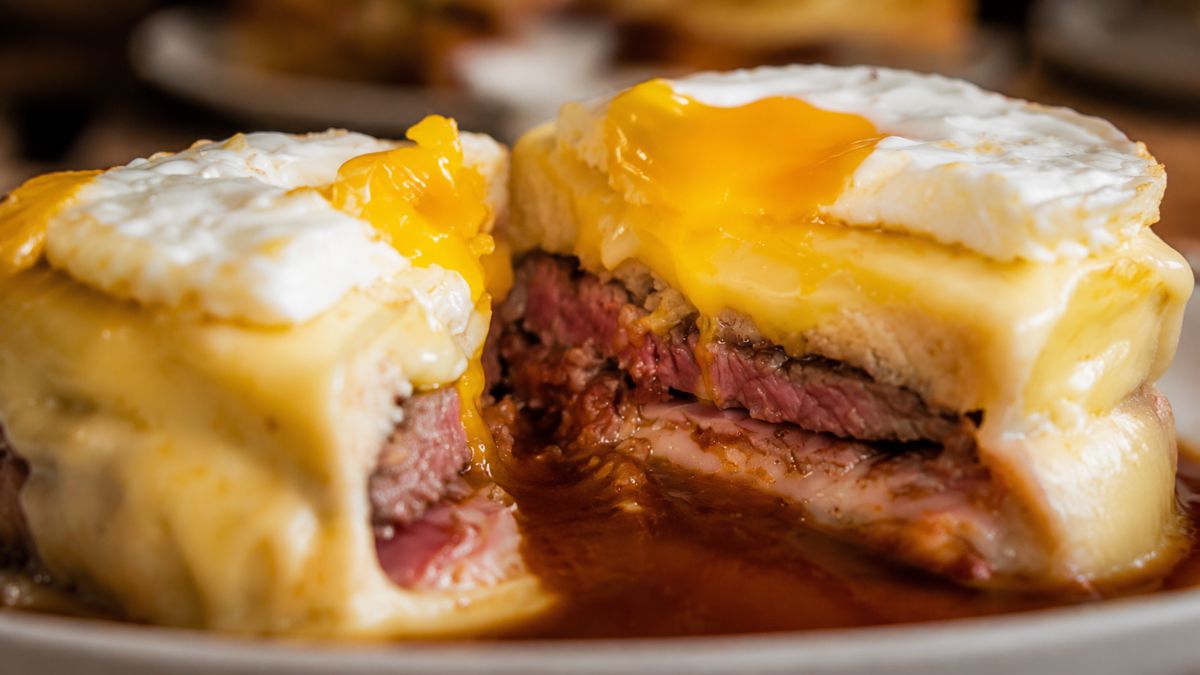 Francesinha tradicional portuense cortada ao meio mostrando o recheio de carne o queijo derretido a gema de ovo e o molho denso.