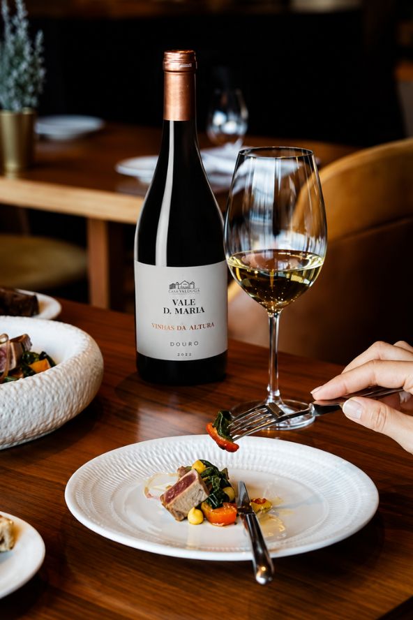 Garrafa de vinho branco Vale D. Maria Douro ao lado de taça e prato gourmet de atum selado com legumes em restaurante sofisticado de gastronomia portuguesa.