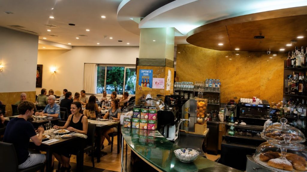 Salão interno do restaurante Mestre d’Aviz no Porto com clientes almoçando em mesas escuras ao lado do balcão principal.