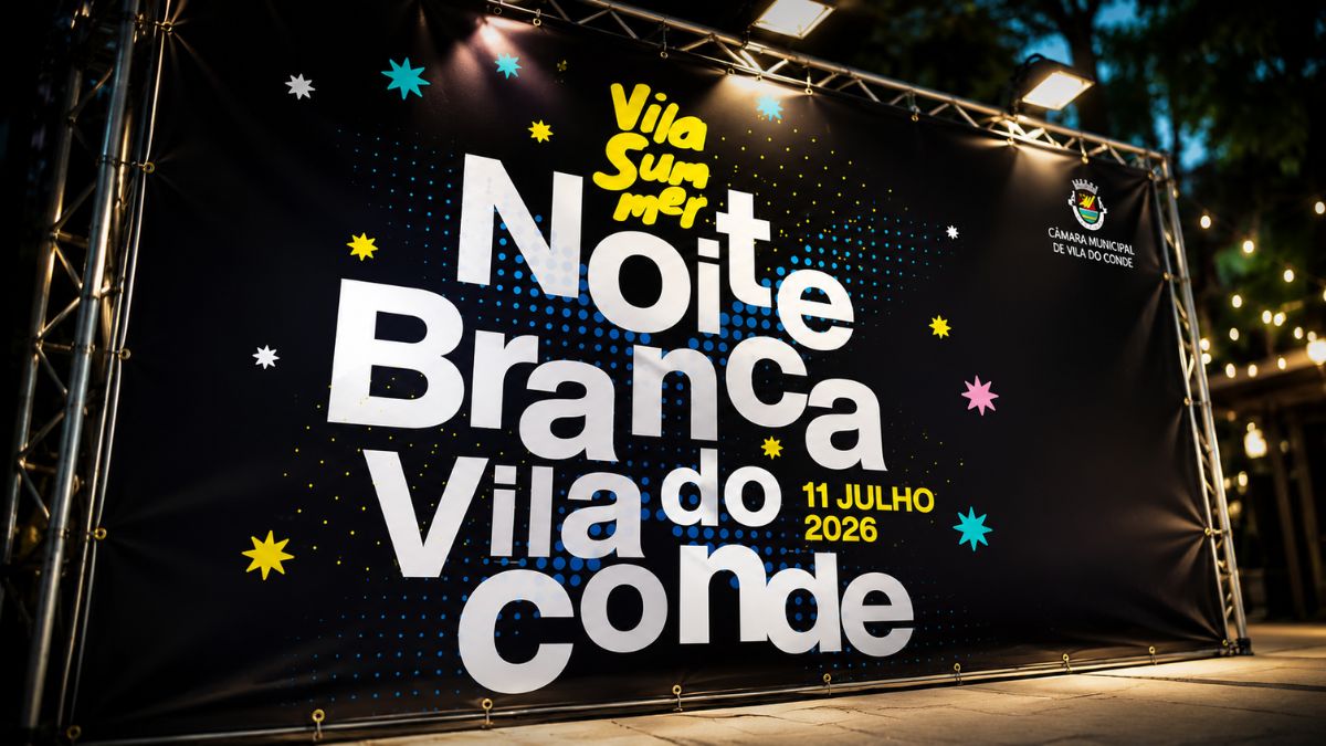 Grande lona publicitária preta montada num suporte de metal ao ar livre durante o entardecer. O painel exibe letras brancas e amarelas com informações sobre o evento festivo de verão, iluminado por projetores de luz fixados no topo da estrutura.