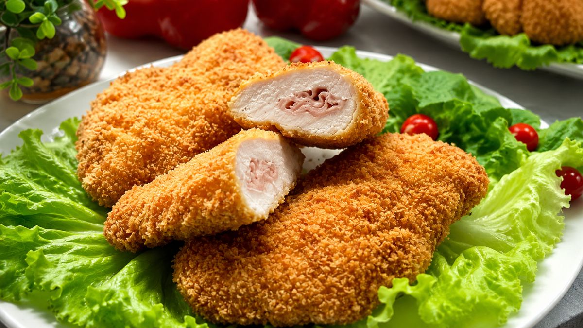 Prato com peito de frango empanado crocante e recheado com presunto, servido sobre folhas verdes de alface e tomate cereja.
