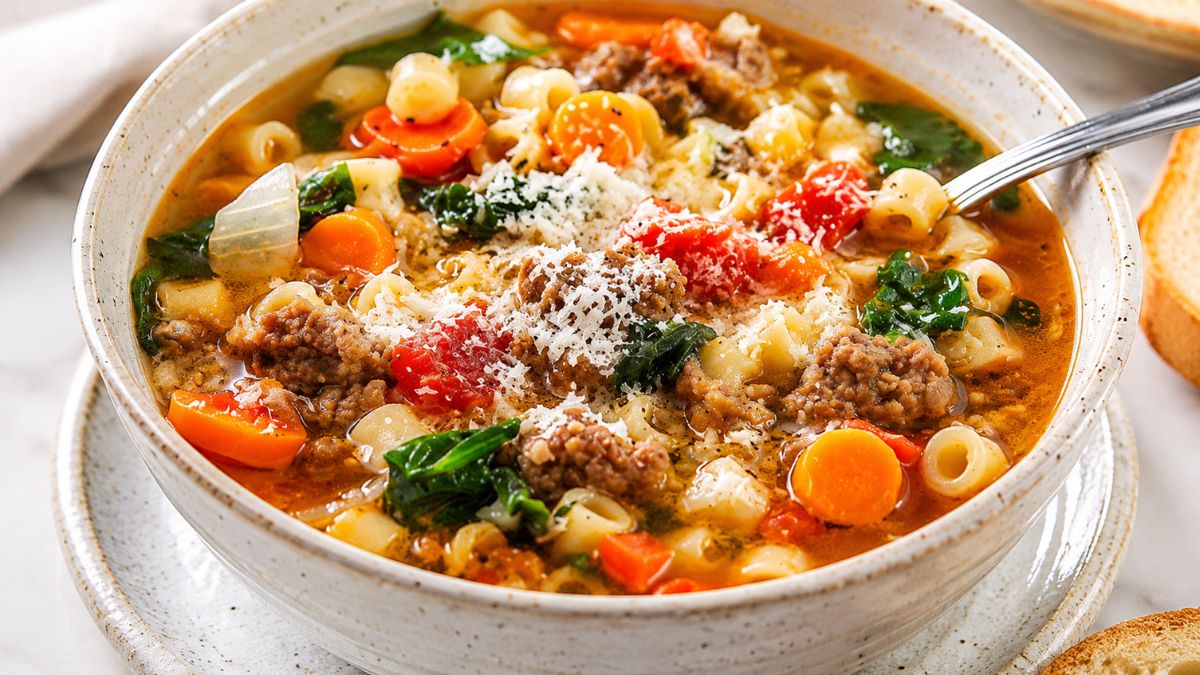 Tigela funda de cerâmica com sopa quente de carne moída, massa curta, cenoura, espinafre e queijo ralado por cima.
