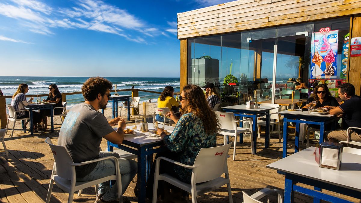 Pessoas almoçando no deck de madeira de um restaurante à beira-mar com vista para o oceano na Costa Nova Aveiro.