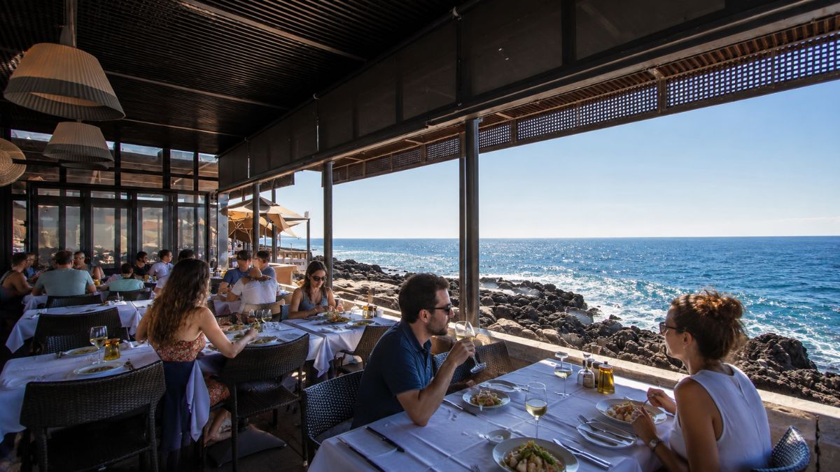 Pessoas almoçando em uma varanda coberta de restaurante à beira-mar, com mesas postas e vista direta para o oceano e formações rochosas em Cascais.