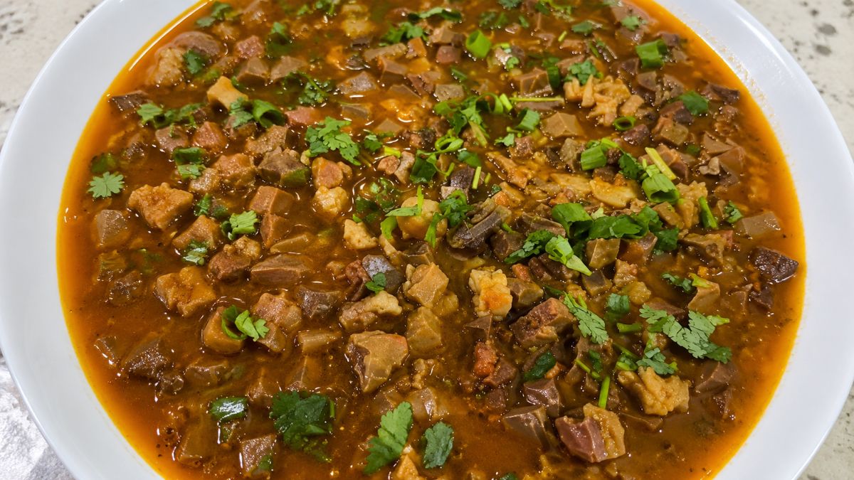 Prato fundo branco servido com sarapatel de porco caseiro em caldo apurado, repleto de miúdos em cubos e finalizado com coentro e cebolinha picados.