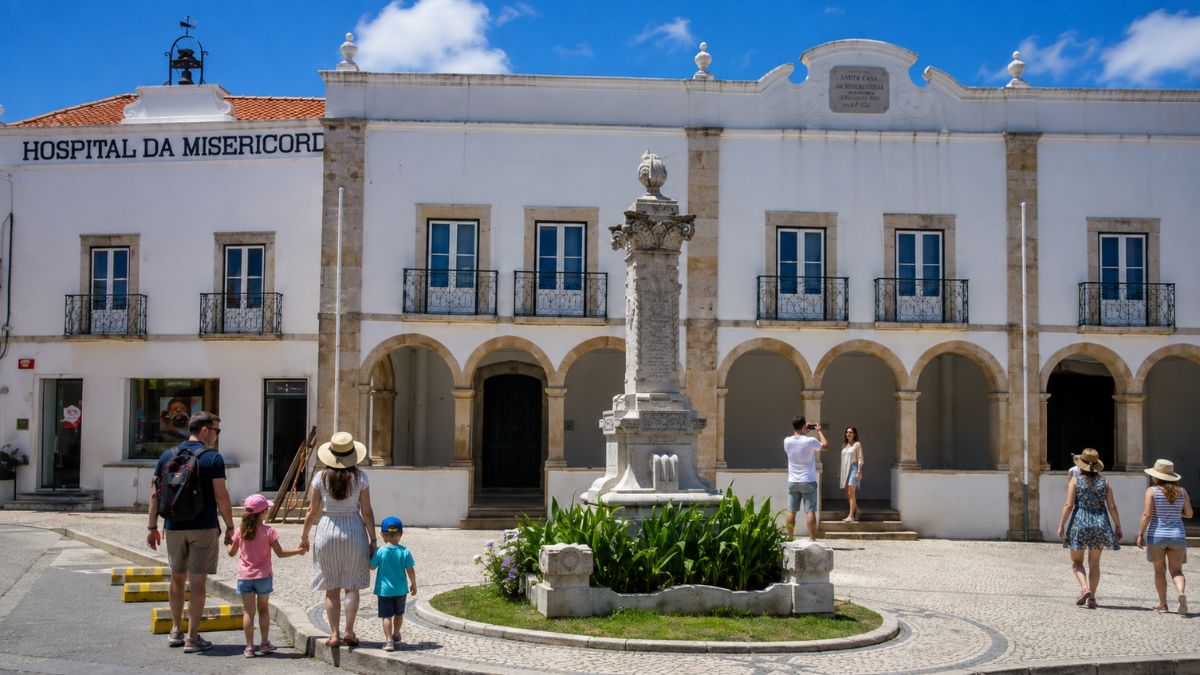 Moradores arrudenses e visitantes caminhando na praça central de Arruda dos Vinhos em frente ao edifício histórico do Hospital da Misericórdia.