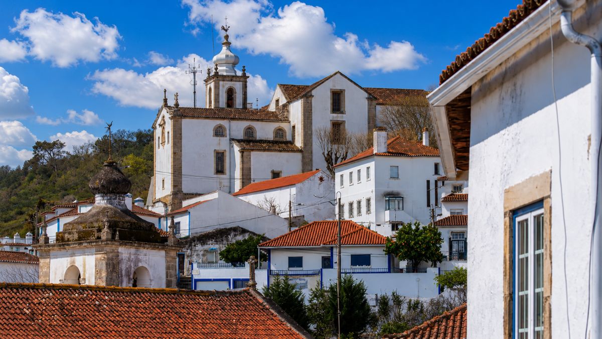 Perspetiva dos telhados de telha tradicional e casas brancas de Alenquer com a igreja e torre sineira do Convento de São Francisco ao fundo.