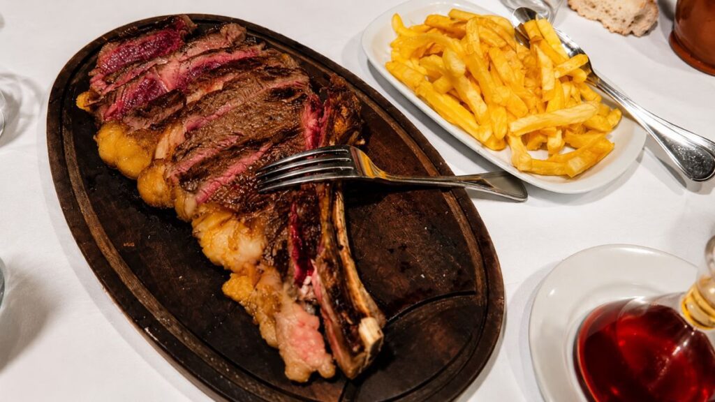 Costeletão de vaca fatiado em tábua de madeira ao lado de travessa de batatas fritas no Restaurante O Fuso em Arruda dos Vinhos.