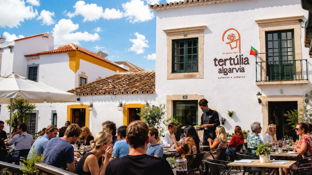 Clientes almoçando na área externa do restaurante Tertúlia Algarvia diante de um prédio histórico branco no centro antigo de Faro.