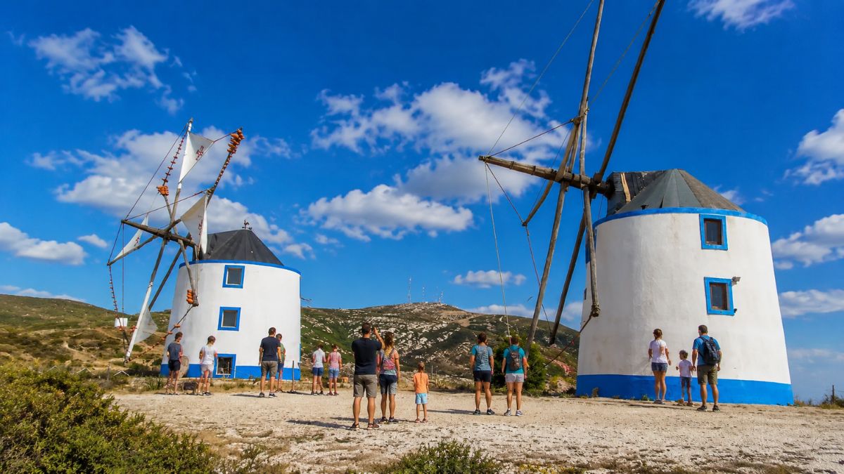 Grupo de visitantes e famílias a contemplar os tradicionais moinhos de vento brancos e azuis de Avis em Alenquer sob céu ensolarado.