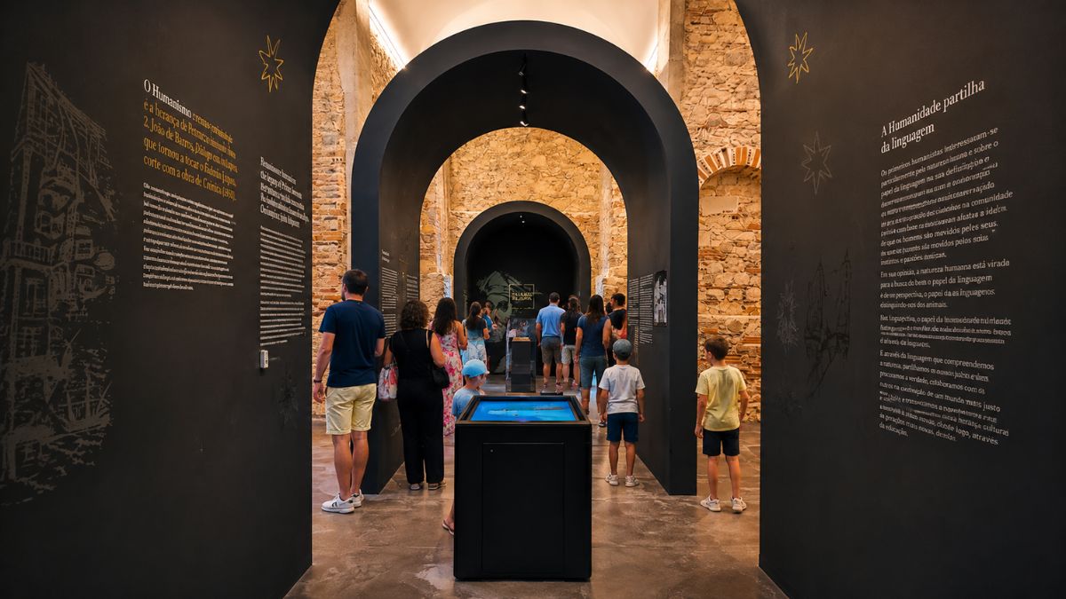 Interior moderno do Museu Damião de Góis em Alenquer com visitantes a observar painéis expositivos e arcos históricos em pedra.