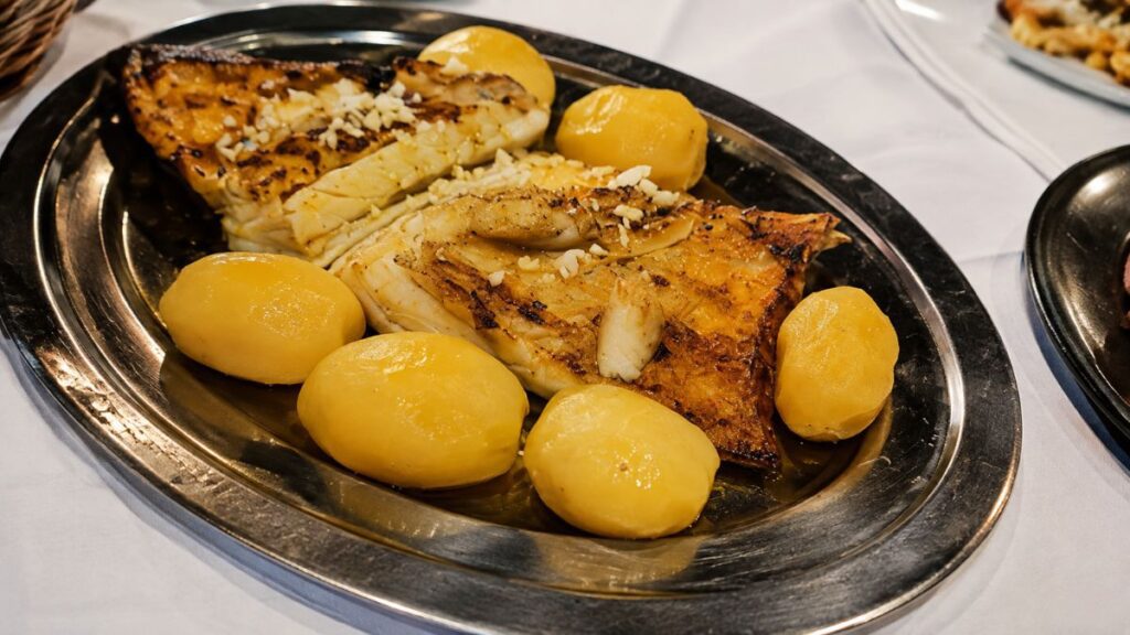 Travessa de inox com generosas postas de bacalhau grelhado com alho e batatas cozidas do Restaurante O Fuso em Arruda dos Vinhos.