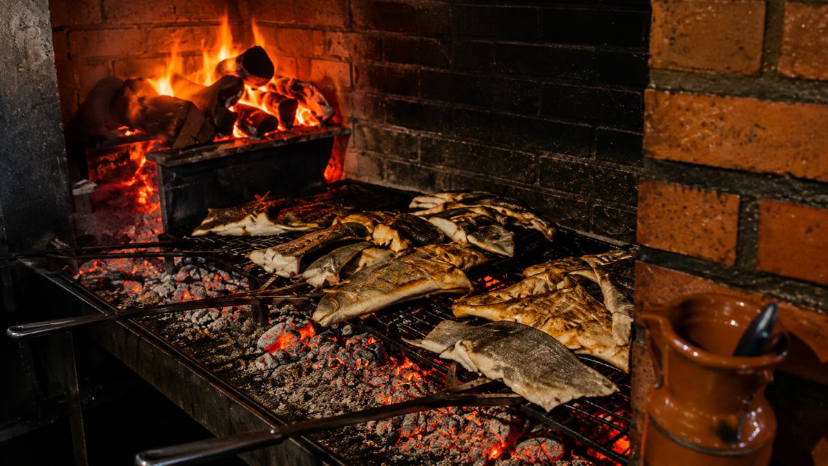 Grandes postas de bacalhau sendo assadas na grelha sobre brasas intensas na churrasqueira do Restaurante O Fuso em Arruda dos Vinhos.