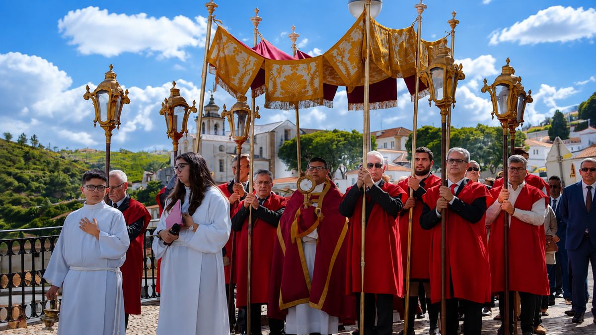 Procissão religiosa em Alenquer com o pároco sob um pálio dourado acompanhado por elementos da irmandade com capas vermelhas.