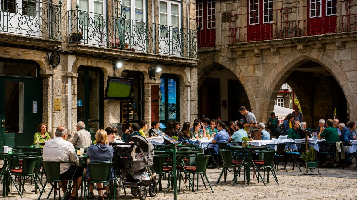 Esplanada movimentada de restaurante no centro histórico de Guimarães em praça de pedra medieval com arcos e prédios antigos em Portugal.