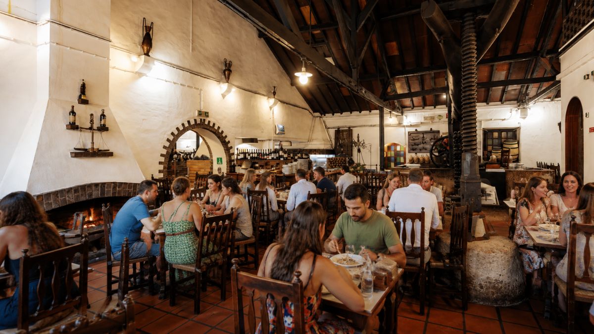 Fotografia do salão interno rústico do Restaurante O Fuso em Arruda dos Vinhos, destacando a grande prensa histórica de madeira e clientes em mesas.