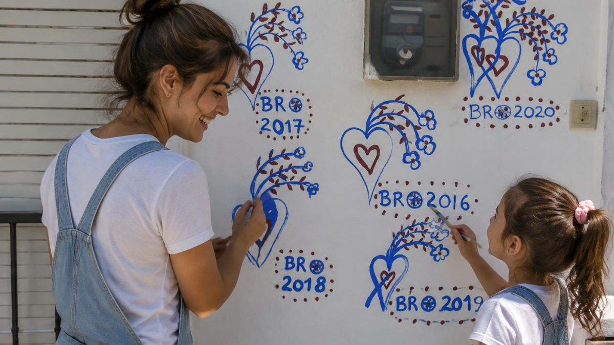Mulher e criança a pintar corações e flores em azul e vermelho na parede branca de uma casa celebrando a tradição dos Reis em Alenquer.